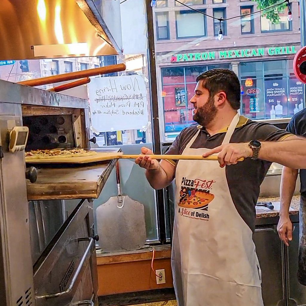 A;ex Making Pizza at Slice on Broadway. Sliding the pizza into the oven off the pizza peel.