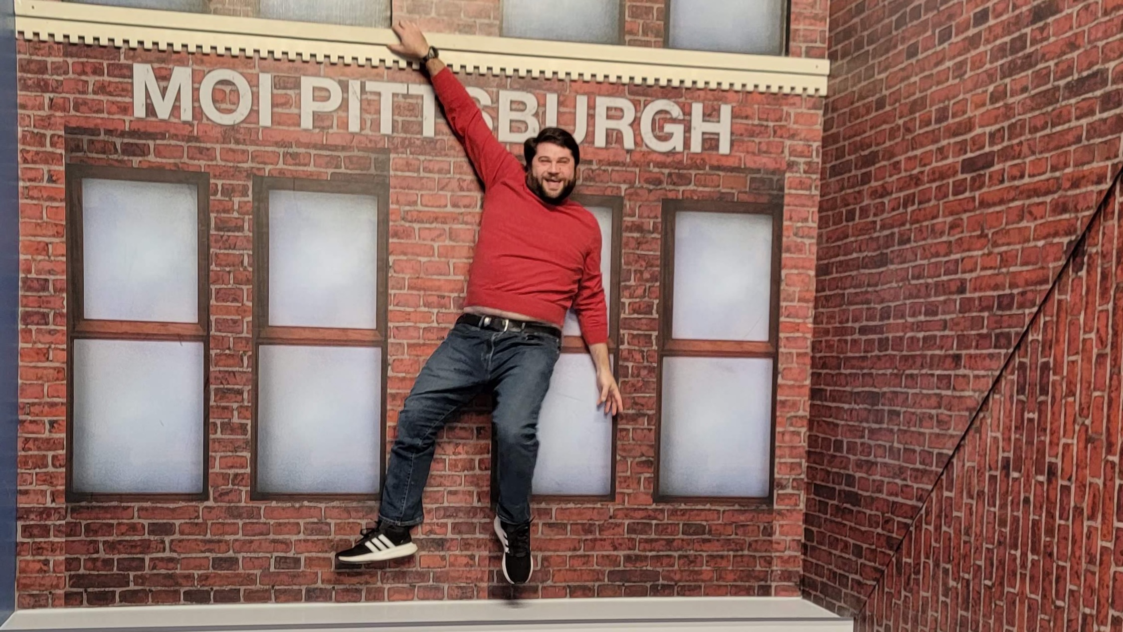 Alex at the Museum of Illusions Pittsburgh doing a hanging from a building illusion