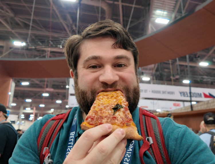 Alex is eating a slice of pizza at the International Pizza Expo