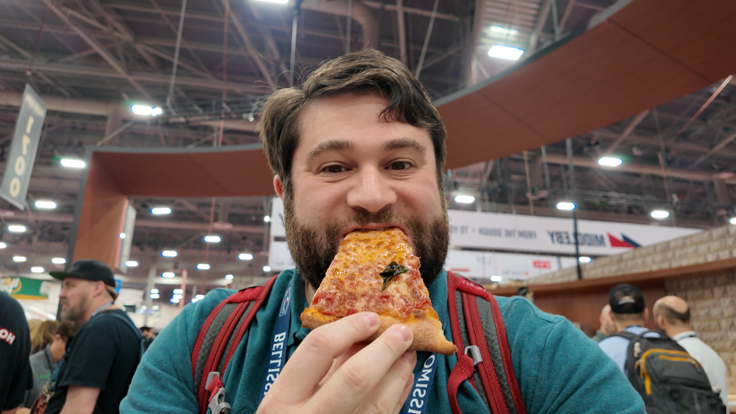 Alex is eating a slice of pizza at the International Pizza Expo