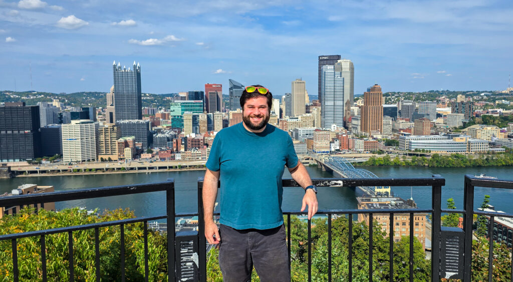 Alex standing at the Mon Incline Overlook in Mt Washington Pittsburgh with the Pittsburgh skyline in the background