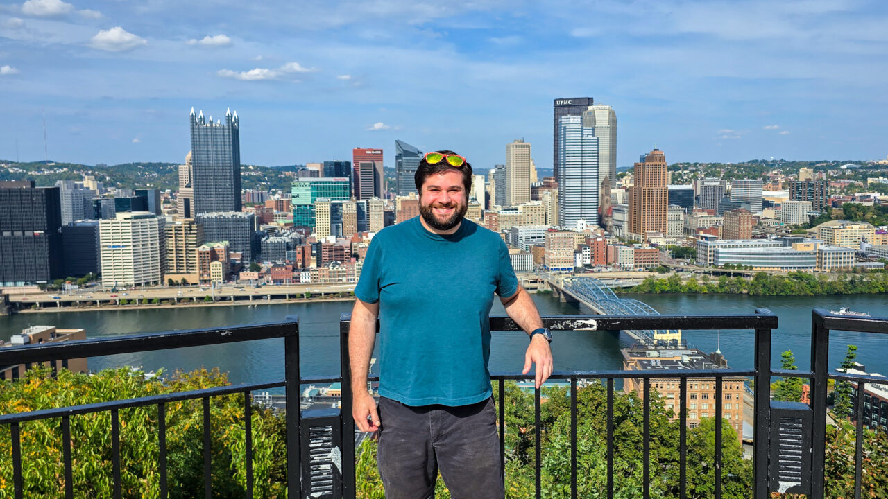 Alex standing at the Mon Incline Overlook in Mt Washington Pittsburgh with the Pittsburgh skyline in the background