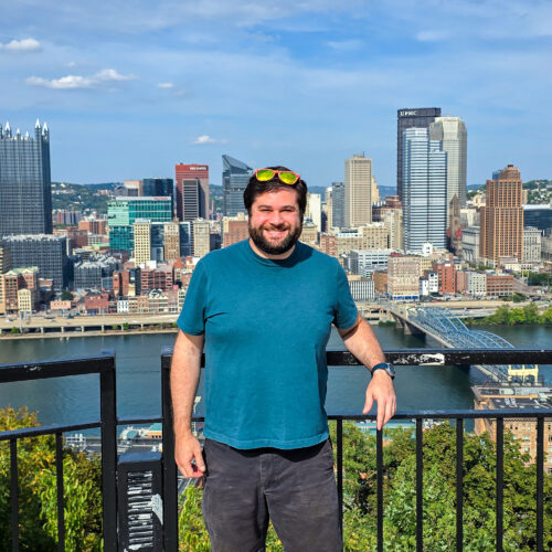 Alex standing at the Mon Incline Overlook in Mt Washington Pittsburgh with the Pittsburgh skyline in the background