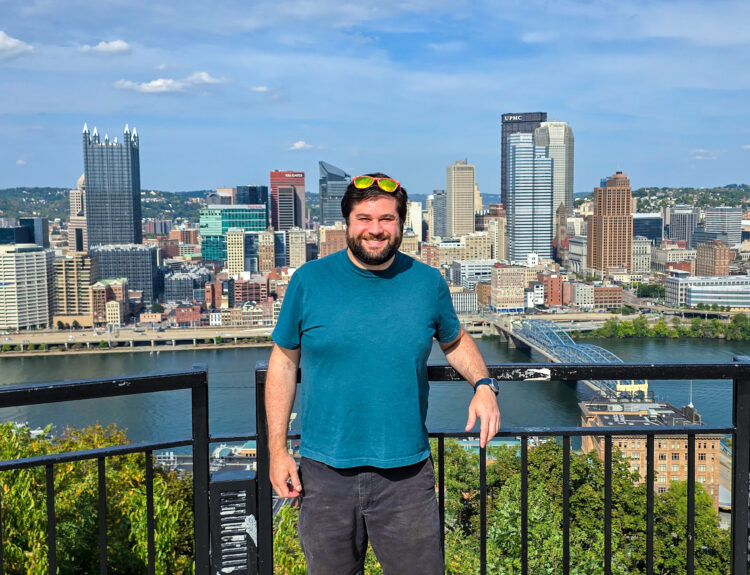 Alex standing at the Mon Incline Overlook in Mt Washington Pittsburgh with the Pittsburgh skyline in the background
