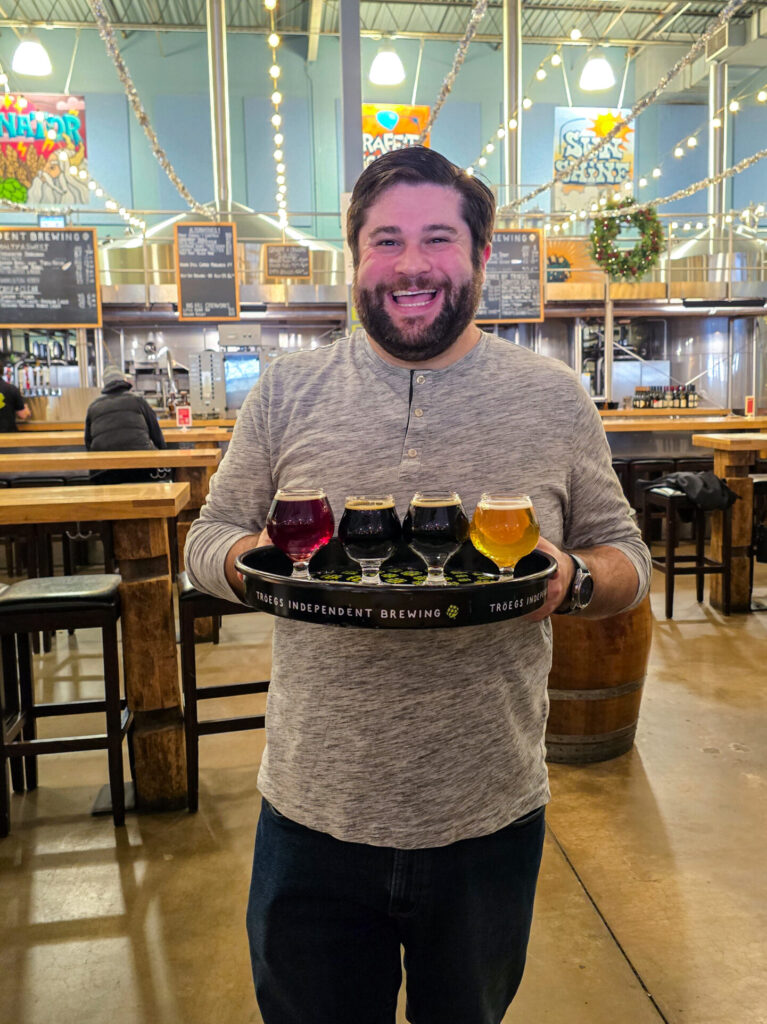 Alex holding a tray with a flight of four 4 oz beers at Troegs Independent Brewing