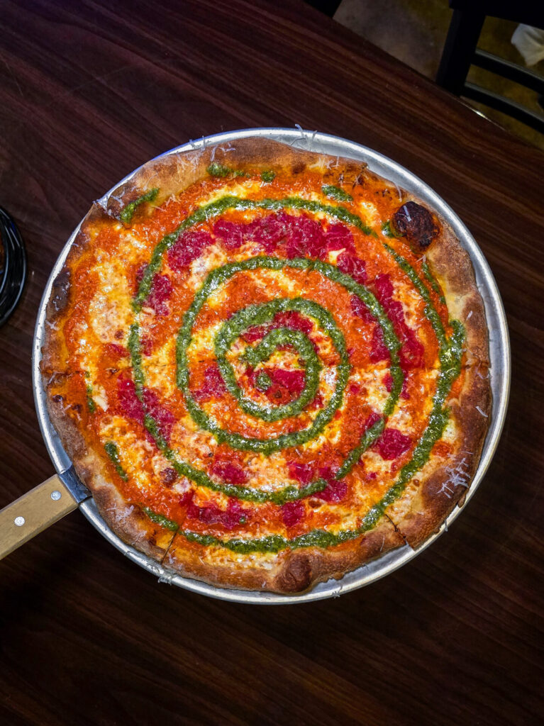 Yellow Bridge Brewing Tie Dye Pizza is a round pizza with swirls of vodka sauce, marinara sauce and pesto sauce.