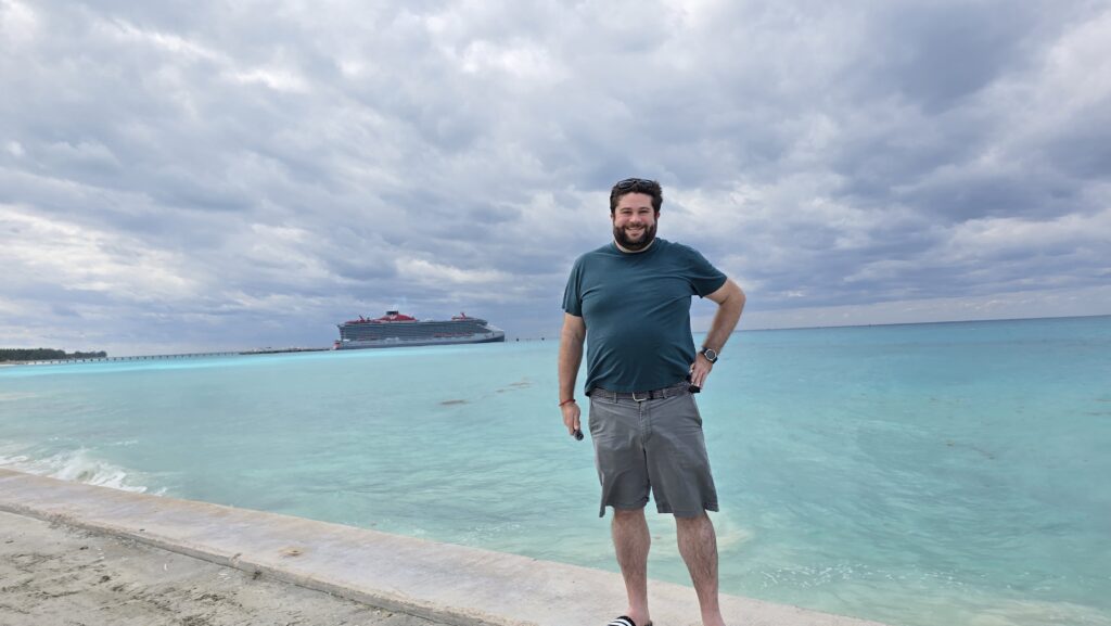 Alex with the Virgin Voyages Scarlet Lady cruise ship in the distance 