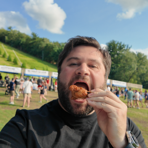 Alex at Tussey Mountain WingFest eating a chicken wing drumstick with the vendor booths in the background