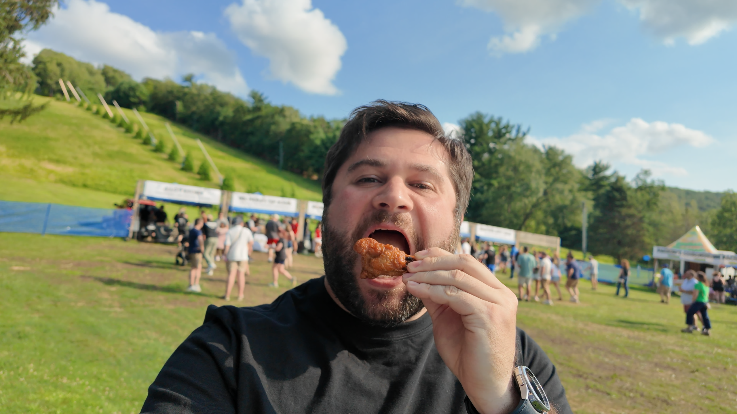 Alex at Tussey Mountain WingFest eating a chicken wing drumstick with the vendor booths in the background